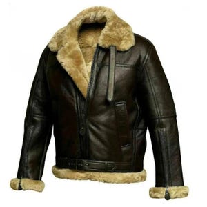 Puede incluir: Chaqueta de cuero marrón oscuro con cuello y forro de borrego beige. La chaqueta tiene cremallera frontal, cinturón con hebilla en la cintura y ribete de borrego en los puños. Estilo aviador clásico.
