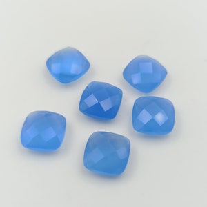 May include: Six faceted, square-shaped, light blue gemstones are arranged on a white surface. The gems have a cushion cut with multiple facets that catch the light, creating a sparkling effect. The color is a soft, sky blue.