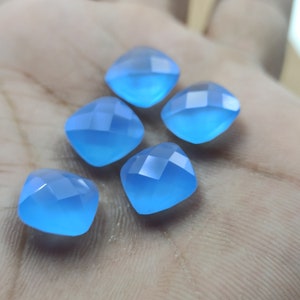 May include: Five faceted, square-shaped, light blue gemstones. The gems have a soft, translucent appearance and are arranged on a neutral background. The facets catch the light, creating a subtle sparkle. These gemstones could be used for jewelry making.