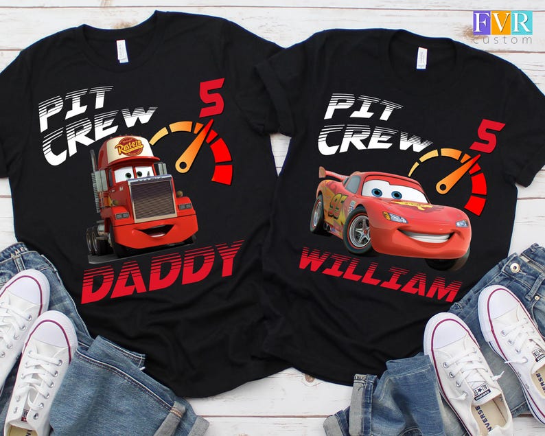 May include: Black t-shirts featuring the text "PIT CREW" and a speedometer graphic. One shirt has a red cartoon truck with "DADDY" below, the other has a red race car with "WILLIAM" below. Both have the number 5.