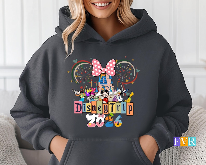 Puede incluir: Sudadera con capucha gris oscuro con un dise&ntilde;o colorido de Disney Trip 2023. El dise&ntilde;o incluye un lazo rosa con lunares, un castillo, fuegos artificiales y varios personajes de Disney. La sudadera tiene una capucha con cord&oacute;n y un bolsillo delantero.