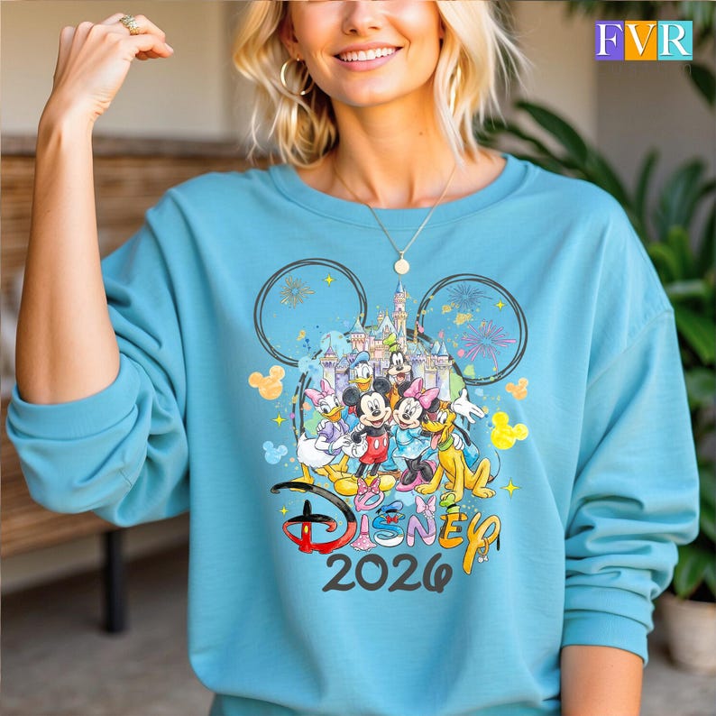 May include: A turquoise sweatshirt with a Disney design. The design features Mickey Mouse, Minnie Mouse, Donald Duck, Daisy Duck, Goofy, and Pluto, a castle, fireworks, and the text "Disney 2026".