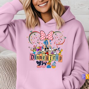 Puede incluir: Sudadera con capucha rosa claro con un dise&ntilde;o de Disney Trip 2023. El dise&ntilde;o incluye a Mickey y Minnie Mouse, otros personajes de Disney, un lazo de lunares y una ilustraci&oacute;n de castillo.