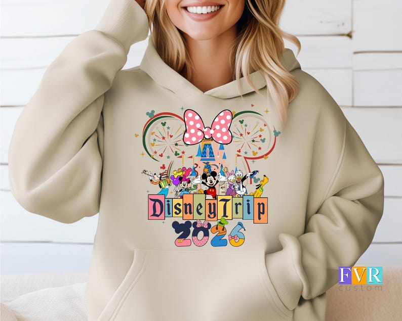 Puede incluir: Sudadera con capucha beige con un dise&ntilde;o de Disney Trip 2023. El dise&ntilde;o incluye a Mickey y Minnie Mouse, otros personajes de Disney, un lazo rosa con lunares y un castillo. La sudadera tiene un bolsillo delantero y una capucha con cord&oacute;n.