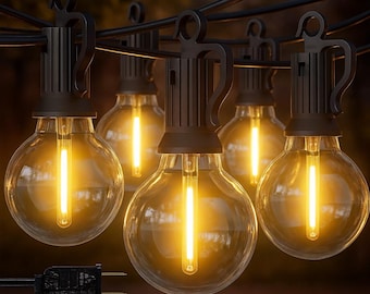 May include: String of outdoor globe string lights. Each light has a clear, round bulb with a warm yellow glow. The bulbs are connected by a black wire and have a black fixture. A black plug is visible at the end of the string.