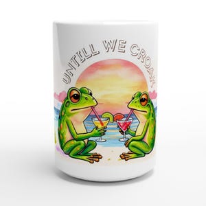 Puede incluir: Taza de cerámica blanca con dos ranas verdes bebiendo cócteles en una playa, con una puesta de sol de fondo. La taza tiene el texto "UNTILL WE CROAK". Las ranas sostienen copas de cóctel con pajitas.