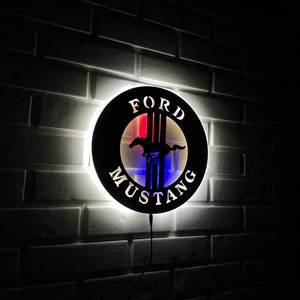 May include: A black metal wall sign with a white halo light. The sign features the Ford Mustang logo with the words "FORD" and "MUSTANG" in white lettering.