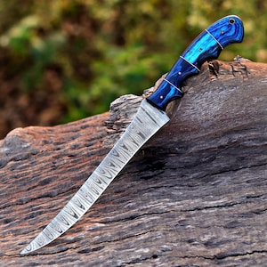 May include: A fixed-blade knife featuring a long, slender blade with a distinct wavy Damascus steel pattern. The handle is crafted from polished blue wood with a swirling grain, secured by three small metal pins and a lanyard hole at the end.