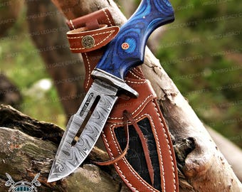 May include: A Damascus steel hunting knife with a blue wooden handle and a brown leather sheath. The blade has a unique pattern, and the handle features a decorative pin. The sheath has a belt loop and decorative stitching.