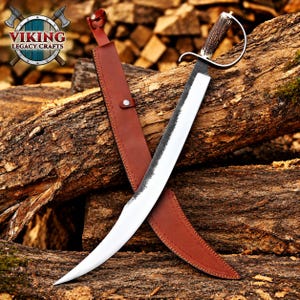 May include: A curved steel blade with a textured dark spine and a polished edge, featuring a handle made of textured brown antler with a metal guard. The sword is accompanied by a brown leather sheath with a metal snap closure and strap.