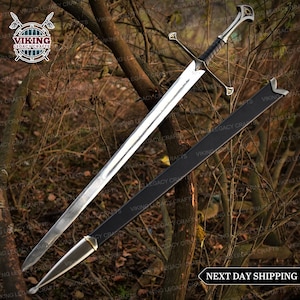 May include: A long, silver sword with a black handle and crossguard, in a black sheath. The double-edged blade has decorative elements on the hilt. The image includes the text "NEXT DAY SHIPPING".