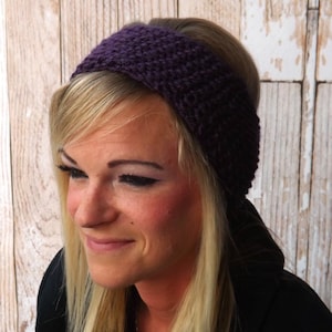 May include: A purple knitted headband worn by a person with blonde hair. The headband is thick and has a simple knit pattern.