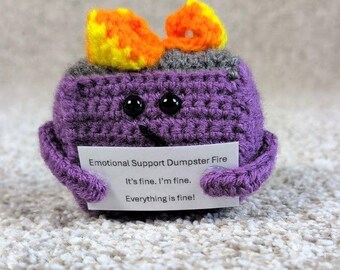 May include: A handmade purple crochet figure resembling a dumpster with flames on top. The figure has black button eyes and holds a sign that reads "Emotional Support Dumpster Fire. It's fine. I'm fine. Everything is fine!"