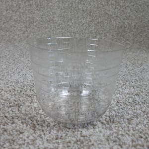 May include: A clear, transparent plastic measuring cup featuring horizontal graduation lines etched into the exterior surface. The cup has a wide, open top and a rounded base, designed for measuring liquid or dry ingredients in a kitchen setting.