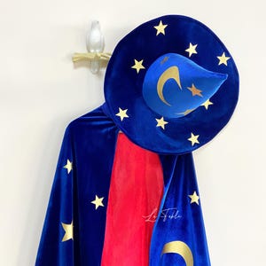 May include: A blue velvet wizard's cape with gold stars and a crescent moon design. The cape is paired with a matching blue velvet hat with gold stars and a crescent moon.