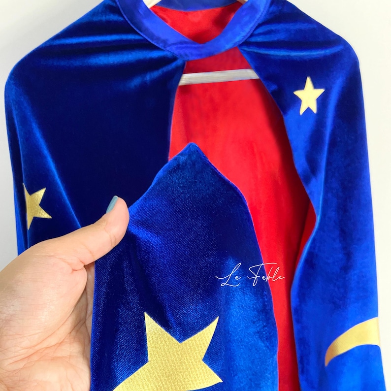 May include: A blue velvet cape with gold stars and a red lining. The cape has a high collar and is perfect for dressing up as a superhero.