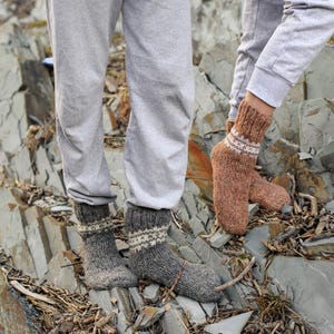 Puede incluir: Dos pares de calcetines de lana en marr&oacute;n y gris con detalles blancos. Los calcetines los llevan dos personas de pie sobre una superficie rocosa.