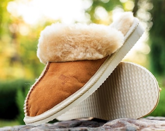 May include: A pair of brown suede slippers with a cream-colored sole and a fluffy, light brown shearling lining. The slippers are designed for indoor wear and offer warmth and comfort.