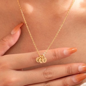 Puede incluir: Un collar de cadena de oro con tres pequeños discos de oro colgando de él. Cada disco tiene una letra grabada: A, N y P.