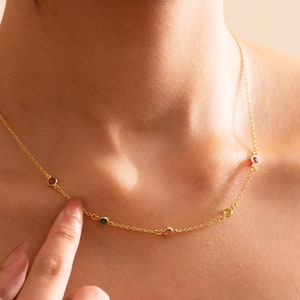 Puede incluir: Un collar de cadena de oro con cinco pequeñas piedras redondas de diferentes colores. Las piedras preciosas son rojas, verdes, rosas y amarillas.