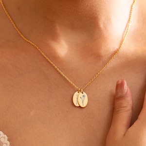 Peut inclure: Collier doré avec deux pendentifs ovales. Chaque pendentif présente un motif floral délicat. Le collier est suspendu à une fine chaîne, créant une esthétique minimaliste et élégante. C'est un bijou.