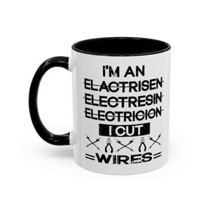 Puede incluir: Taza de café de cerámica blanca con asa negra y borde negro. La taza tiene un gráfico negro que dice "Soy un Elactrisn Electresin Electrición Corto cables" con un par de alicates y rayos.
