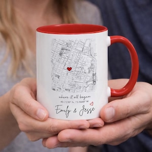 May include: White ceramic mug with a red interior and handle. The mug features a map design with a red heart marking a location. Text on the mug reads "where it all began", coordinates, and the names "Emily & Jesse".