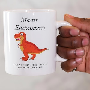 May include: White ceramic coffee mug with a red and orange cartoon dinosaur and the text "Master Electrasaurus. Like a normal electrician, but more awesome."