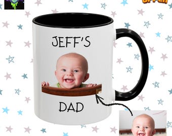 Op de afbeelding: Witte keramische mok met een zwarte binnenkant en handvat. De mok heeft een foto van een lachende baby en de tekst "JEFF'S DAD". Een kleinere afbeelding van de baby is ook inbegrepen. De mok is versierd met een sterrenpatroon.
