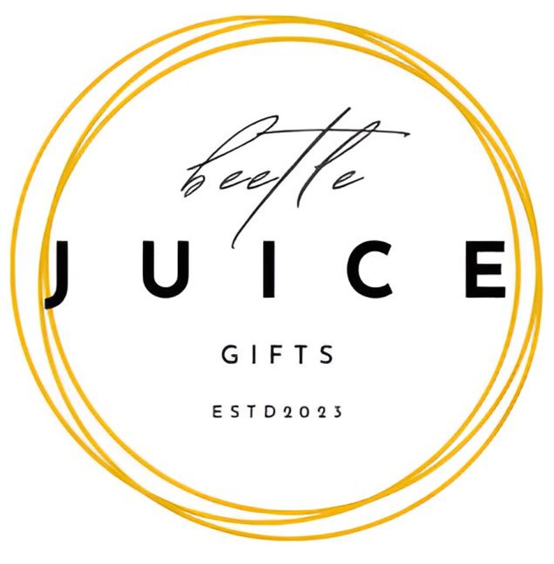 Op de afbeelding: Een gouden cirkel met een dubbele omtrek, de tekst "beetle JUICE GIFTS ESTD 2023" in zwart.