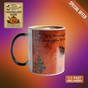 May include: A white Halloween-themed mug with a black handle, filled with a light brown beverage. The mug features a spooky design with a haunted house, bats, and the text "Under the moonlight..." and "Halloween". A sign with a pumpkin is also visible.