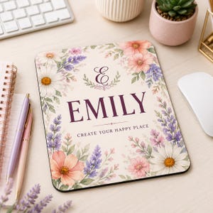 Peut inclure: Un tapis de souris rectangulaire au fond crème orné d'une bordure florale aquarelle composée de marguerites, de lavande et de fleurs pêche. Le centre affiche une lettre E décorative, le nom EMILY en violet foncé et la phrase CREATE YOUR HAPPY PLACE.