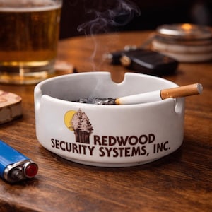 以下が含まれることがあります： 「REDWOOD SECURITY SYSTEMS, INC.」の文字と木と太陽のグラフィックが入った白いセラミック灰皿。 灰皿には火のついたタバコが置かれ、煙が立ち上っています。 青いライターとビールグラスも写っています。