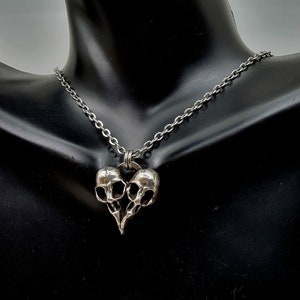 Puede incluir: Un collar de plata con un colgante en forma de dos calaveras unidas en forma de coraz&oacute;n.