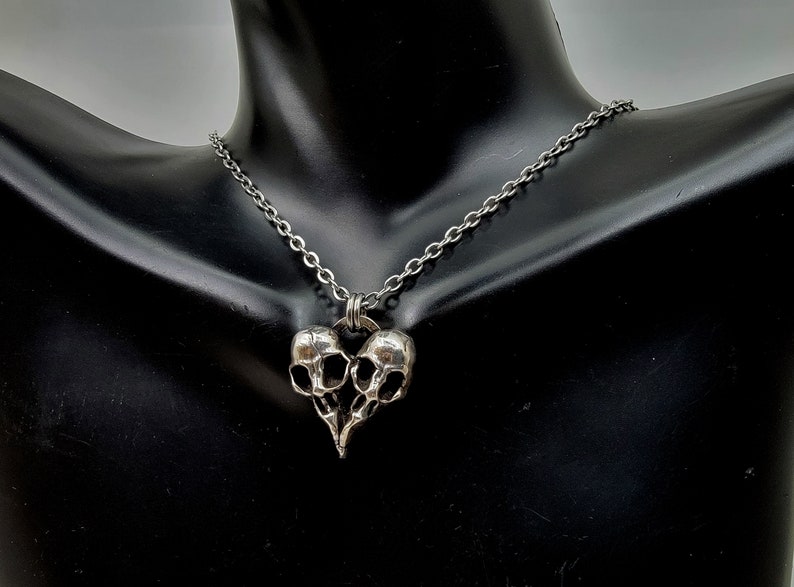 Puede incluir: Un collar de plata con un colgante en forma de dos calaveras unidas en forma de coraz&oacute;n.
