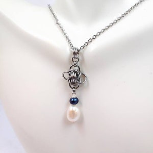 May include: A silver chain necklace with a silver knot pendant and a white pearl drop. The pearl is accented with a small black bead.