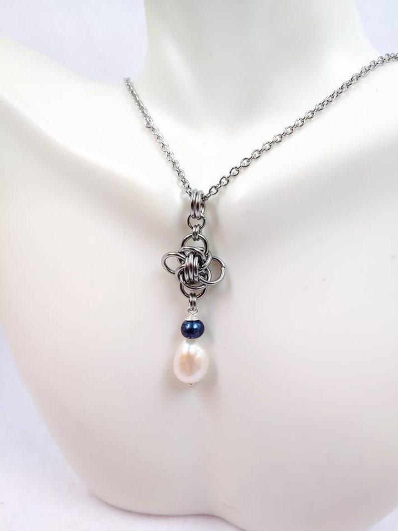 May include: A silver chain necklace with a silver knot pendant and a white pearl drop. The pearl is accented with a small black bead.