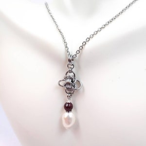 May include: A silver chain necklace with a silver knot pendant and a white pearl and a maroon bead hanging from the knot.