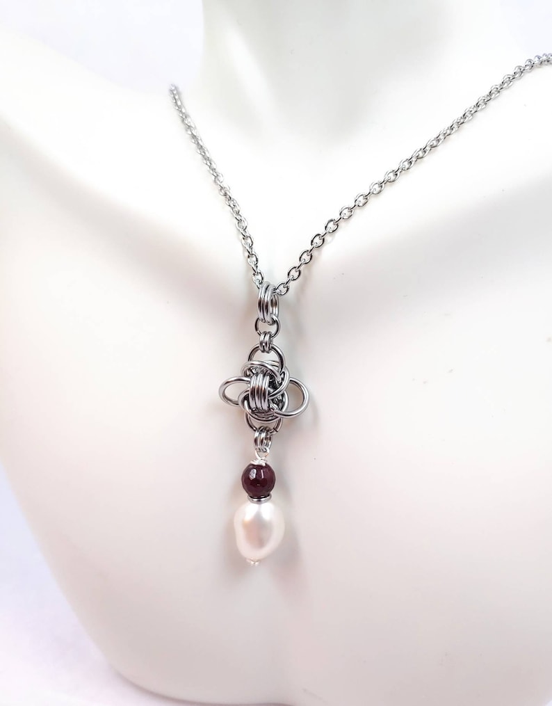 May include: A silver chain necklace with a silver knot pendant and a white pearl and a maroon bead hanging from the knot.