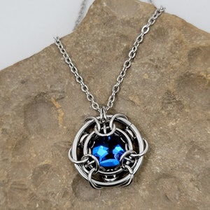 May include: A silver chain necklace with a blue gemstone pendant. The pendant is surrounded by a silver wire cage.