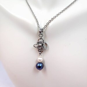 May include: A silver chain necklace with a silver knot pendant and two pearls, one white and one dark blue.