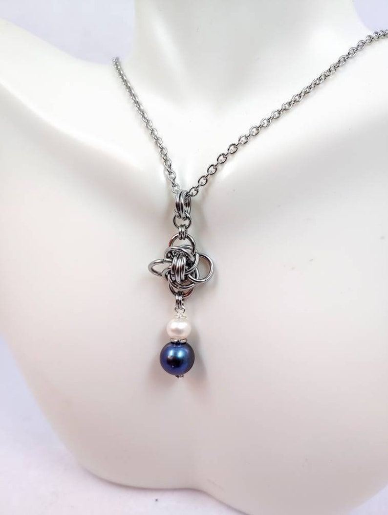 May include: A silver chain necklace with a silver knot pendant and two pearls, one white and one dark blue.