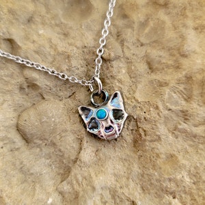 May include: A silver chain necklace with a small silver cat pendant featuring a turquoise gemstone eye.