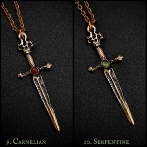 May include: Two bronze sword pendants with different coloured gemstones. The pendant on the left has a red carnelian gemstone, and the pendant on the right has a green serpentine gemstone. Both pendants are on a gold chain.