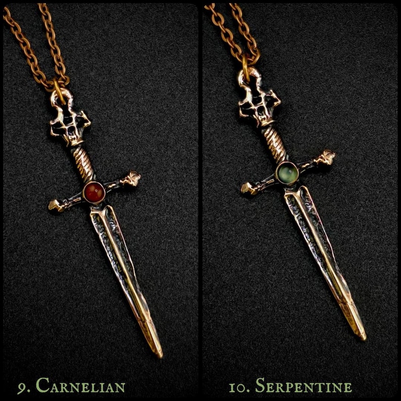 May include: Two bronze sword pendants with different coloured gemstones. The pendant on the left has a red carnelian gemstone, and the pendant on the right has a green serpentine gemstone. Both pendants are on a gold chain.