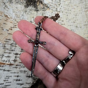 May include: A silver and copper sword pendant with a red gemstone in the centre. The pendant is on a silver chain.