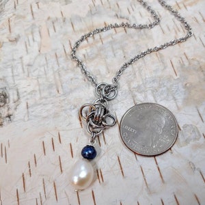 May include: A silver chain necklace with a silver knot pendant and a white pearl and a dark blue bead hanging from the knot.