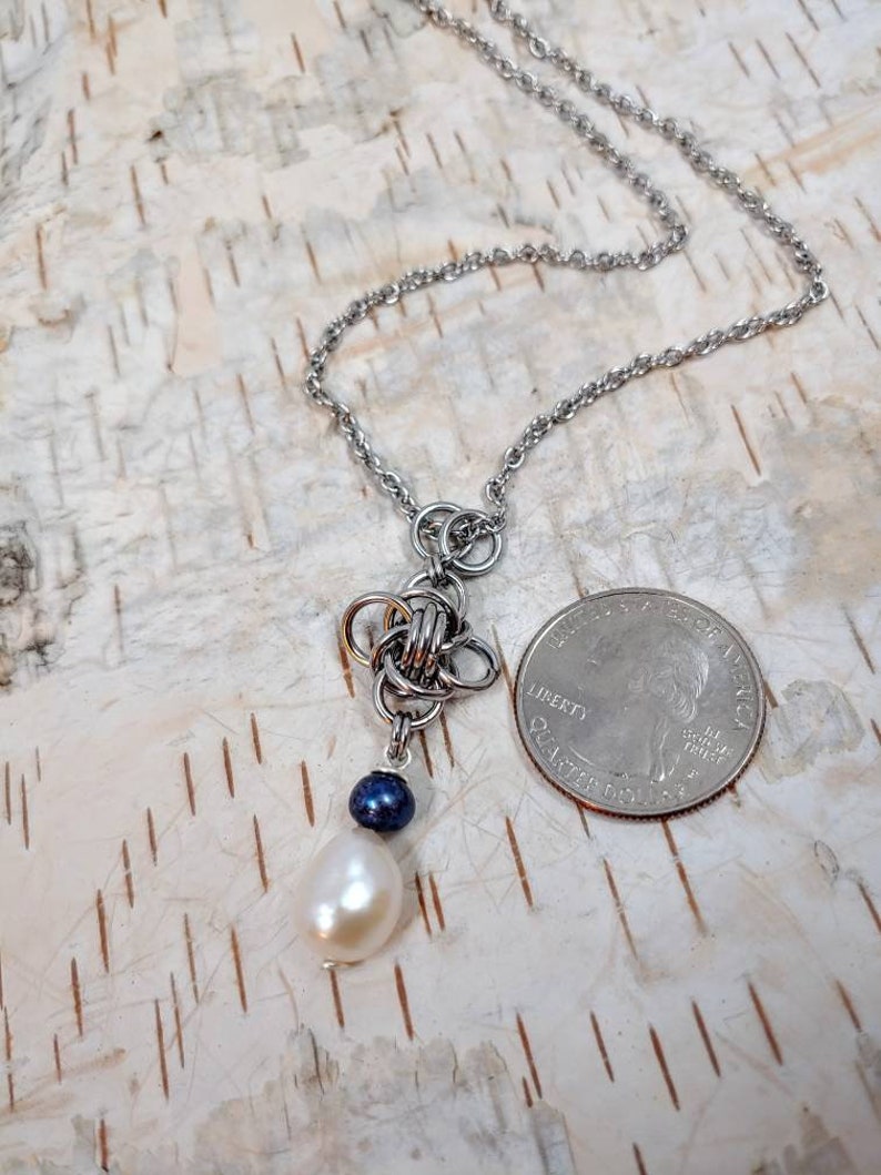 May include: A silver chain necklace with a silver knot pendant and a white pearl and a dark blue bead hanging from the knot.