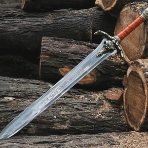May include: A detailed image of a sword with a silver blade and a handle wrapped in red leather. The hilt features a decorative design with a skull motif. The sword rests on a background of stacked logs.