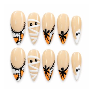 May include: A set of ten almond-shaped press-on nails with a nude base. The designs include black stitched patterns, white mummy bandages with black eyes, orange and black spider web motifs, and white ghost shapes with black eyes on the tips.